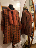 A rust-orange and black patterned knit cardigan with a matching chunky knit scarf displayed on a mannequin in front of a mirror, with a reflection showing the back of the cardigan.
